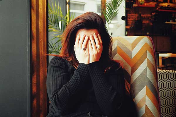 Long haired brunette women covering face with hands in pain